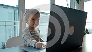 Sweet toddler looks in laptop pushing button on keyboard