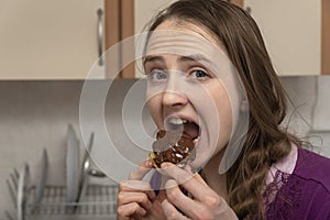 Sweet tooth girl eats eclair with chocolate icing. Forbidden sweets