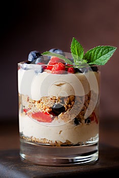 Sweet vegan dessert in a glass with berries, mint, whipped cream and biscuit on a brown background. Healthy food, sugar, gluten