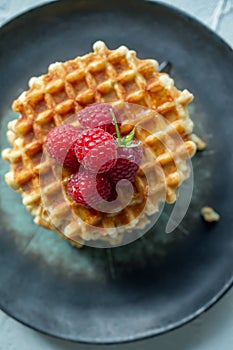 Sweet Viennese waffles with fresh ripe raspberries are served for Breakfast on a beautiful plate. top view. Copy space