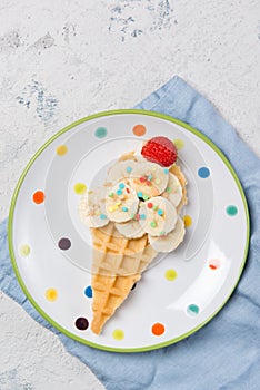 Sweet waffle with banana and strawberry in a shape of ice cream cone, meal for kids idea, top view