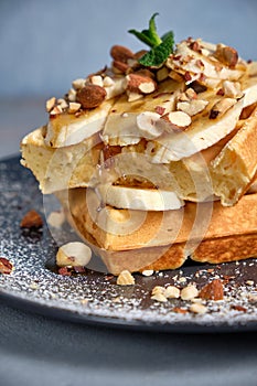 Sweet waffle with caramel and bananas sprinkled with hazelnuts and icing sugar