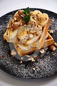 Sweet waffle with caramel and bananas sprinkled with hazelnuts and icing sugar