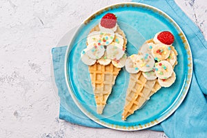 Sweet waffles with banana and strawberry in a shape of ice cream cone, meal for kids idea, top view