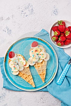 Sweet waffles with banana and strawberry in a shape of ice cream cone, meal for kids idea, top view