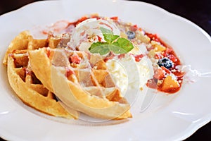 Sweet waffles with strawberries sauce vanilla ice cream fresh fruit and mint leaf on white plate