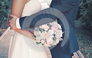 Sweet wedding couple with gentle bouquet of peonies flowers, sensual groom hugging lovely bride