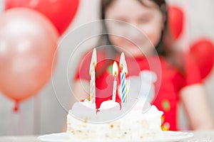 Sweet white birthday cake with candles and defocused happy little girl on the background during party celebration