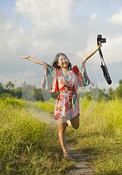 Sweet young Asian Chinese or Korean woman on her 20s posing happy and playful holding photo camera smiling happy in beautiful natu