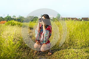 Sweet young Asian Chinese or Korean woman on her 20s taking picture with photo camera smiling happy in beautiful nature landscape