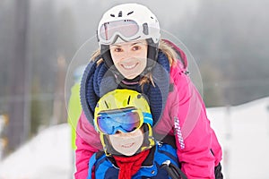 Sweet young boy and his mother, learning to ski on a mild ski slope in Austrian ski resort