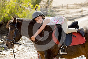 Sweet young girl hugging pony horse smiling happy wearing safety jockey helmet in summer holiday