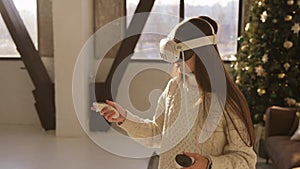 A sweet young lady putting on a virtual reality gear beside a Christmas tree.