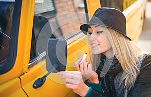 Sweet young woman applies red lipstick looking at the car mirror