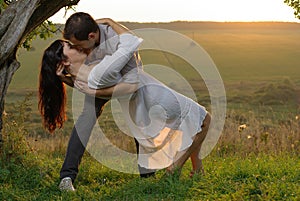 Sweethearts kissing under tree at sunset