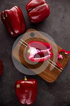 Red bell  peppers on wooden cutting board on black and dark grey background. Green pepper sliced and chopped on wooden chopping