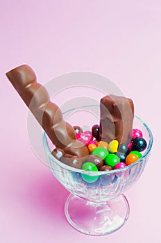 Sweets in a glass vase on a pink background, chocolate bars, colorful candies