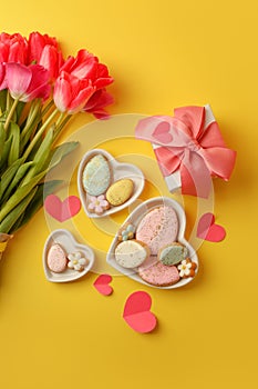 Sweets, pastry, gingerbread cookies for Easter table. Easter eggs heart shaped decor plate, pink tulips on yellow background top