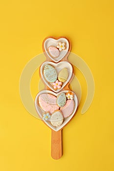 Sweets, pastry, gingerbread cookies for Easter table. Easter eggs heart shaped decor  on yellow background top view copy space,