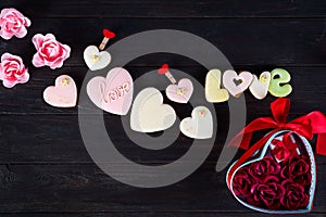 Sweets on Valentine`s Day. Cookies in shape of heart and lettering Love, red hearts shaped and bouquet rose in gift box