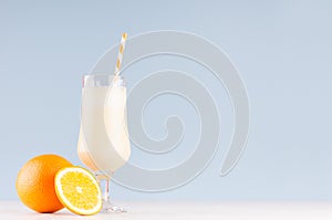 Sweety dairy yogurt of oranges with striped straw, cut orange on soft light blue background.