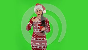 Sweety girl in Santa Claus hat is drinking unpalatable coffee. Green screen
