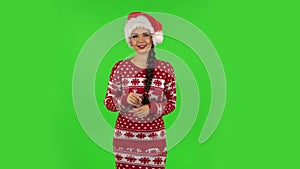 Sweety girl in Santa Claus hat seductively smiling and gesture threatens by shaking her index finger. Green screen