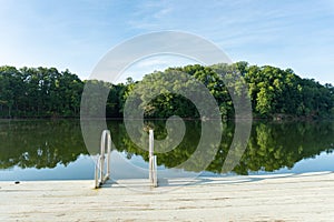 A swim ladder on a dock on Lake Lanier in Georgia with a reflection of green trees in the water