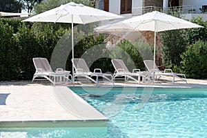 Swim pool with clear blue water and sun beds on sunny day in a yard