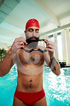 A swimmer in a cap and goggles puts on swimming goggles smiling before swimming training in the pool. Training, training