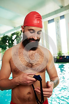 A swimmer in a cap and goggles puts on swimming goggles smiling before swimming training in the pool. Training, training