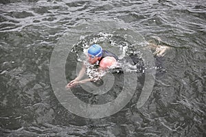 Swimmer in cap and wetsuit performing the breaststroke in dark sea water