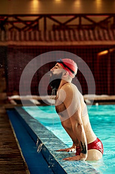 A swimmer in a hat and goggles emerges from the pool exhales water. Training, training or exercises for athletes in