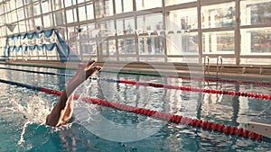 Swimmer at the start jumps into the water in the pool. Water splashes. The camera moves to the right. Slow motion.