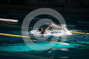 Swimmer swims freestyle in the pool in beautiful sunlight