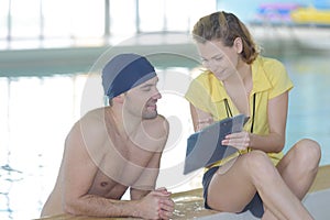 Swimmer talking to coach by poolside at leisure center