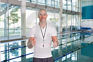 Swimming coach gesturing thumbs up by pool at leisure center