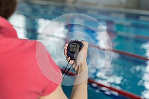 Swimming coach holding stopwatch poolside at the leisure center.