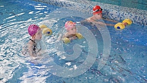 A swimming coach teaches children to swim with foam dumbbells for swimming.