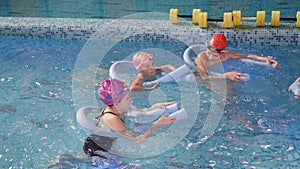 A swimming coach teaches children to swim using foam swimming sticks.