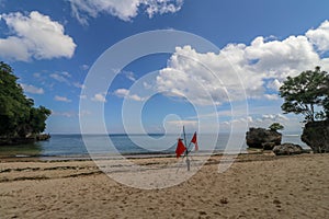 Swimming is dangerous in ocean waves. Red warning flag flapping in the wind on beach at stormy weather