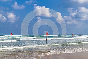 Swimming is dangerous in sea waves. Red warning flag flapping in the wind at stormy weather on the beach