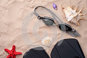 Swimming goggles and flippers on the sand with shells and starfishes.