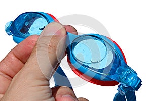 Swimming goggles held in small boy left hand on white background, with drops and traces of salt water on it