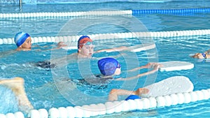 Swimming instructor teaches children to swim in the pool using a swimming board