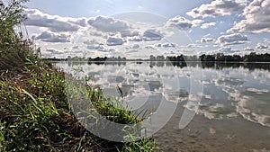 Swimming lake with reflections of the clouds in a light wind and vegetation on the shore