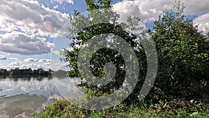 Swimming lake with reflections of the clouds in a light wind and vegetation on the shore