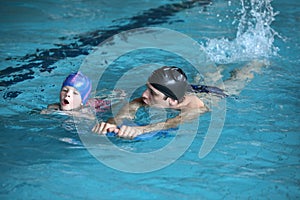 Swimming lesson - child practicing flutter kick with kick board with instructor