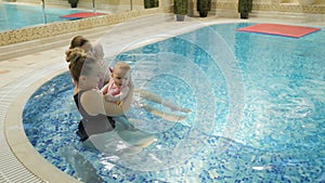 Swimming lesson. Mothers teaching to swim newborn baby at swimming pool