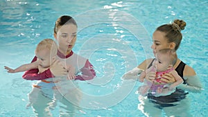 Swimming lesson. Mothers teaching to swim newborn baby at swimming pool